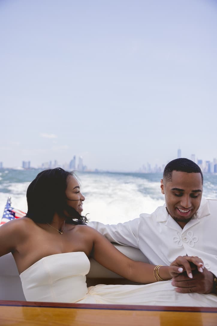 Cayla and Shaddy, dressed in white, hold hands and smile together aboard the boat.