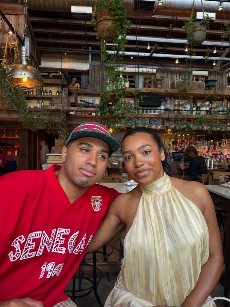 Cayla and Shaddy sit together in a restaurant filled with hanging plants.