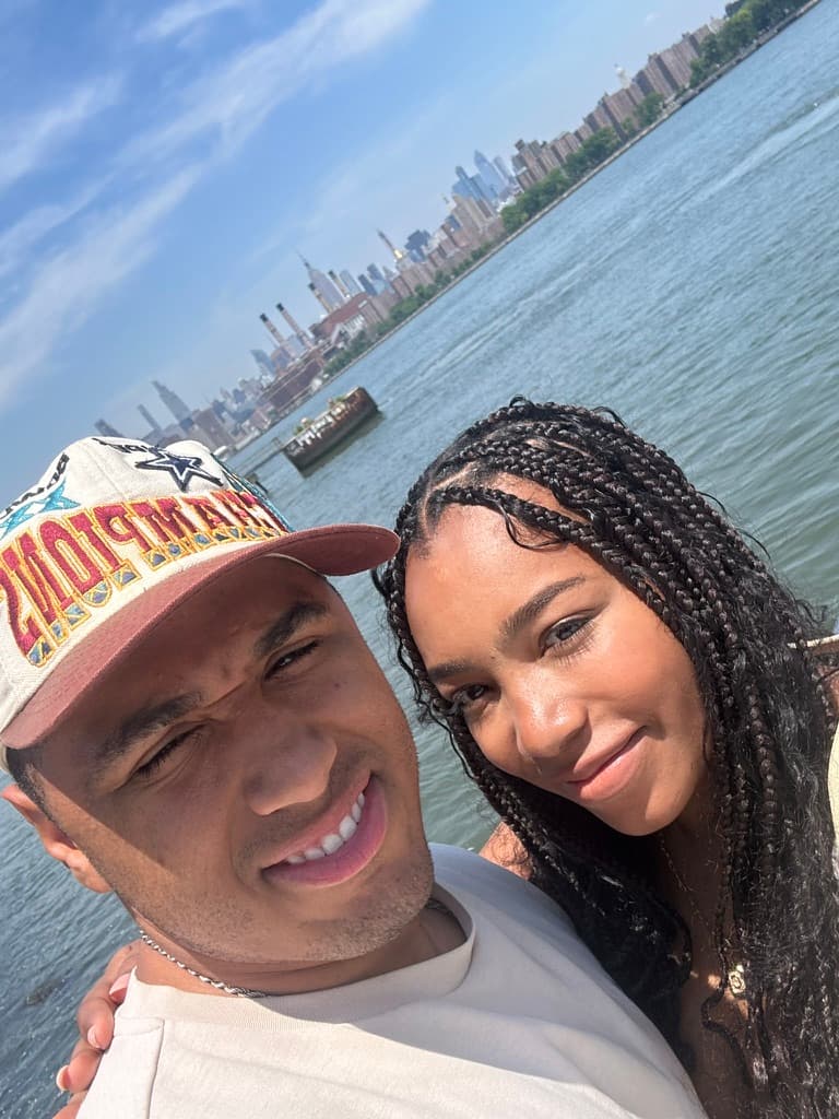 Cayla and Shaddy smiling by the water with the city skyline behind them.