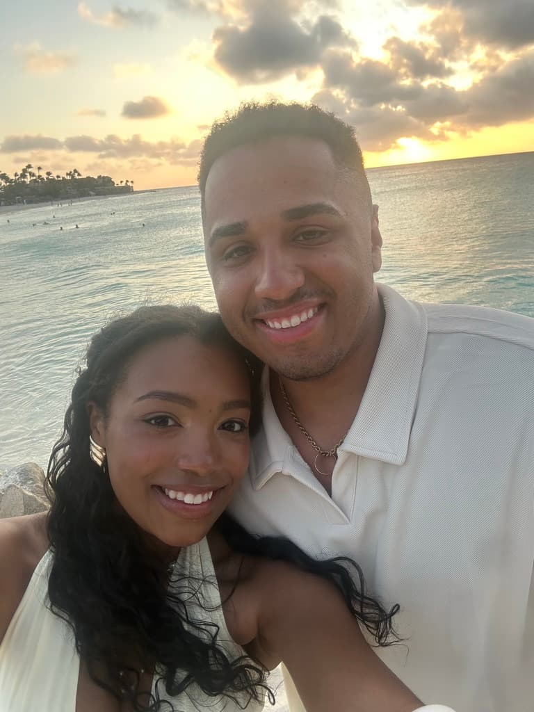 Cayla and Shaddy smile beside the sea at sunset.
