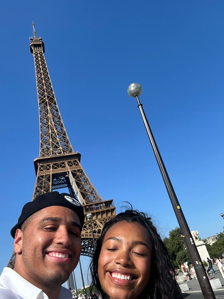 Cayla and Shaddy take a sunlit selfie beneath the Eiffel Tower.