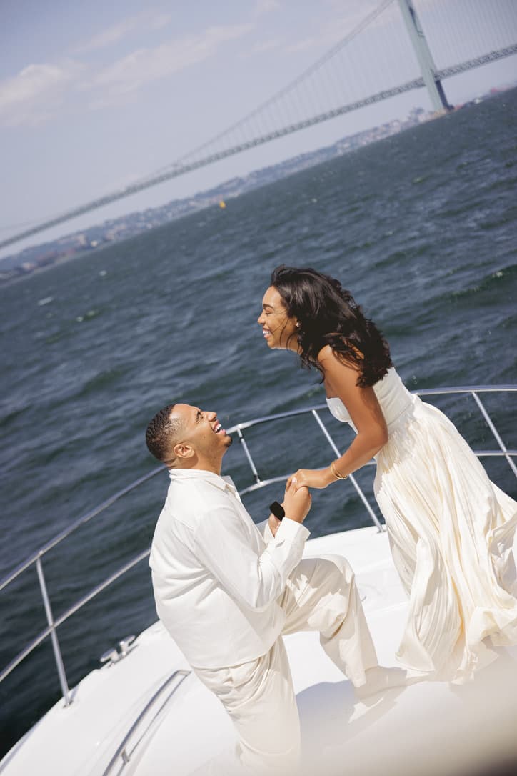 Shaddy kneels with a ring on the bow of a boat as Cayla smiles and holds his hand.
