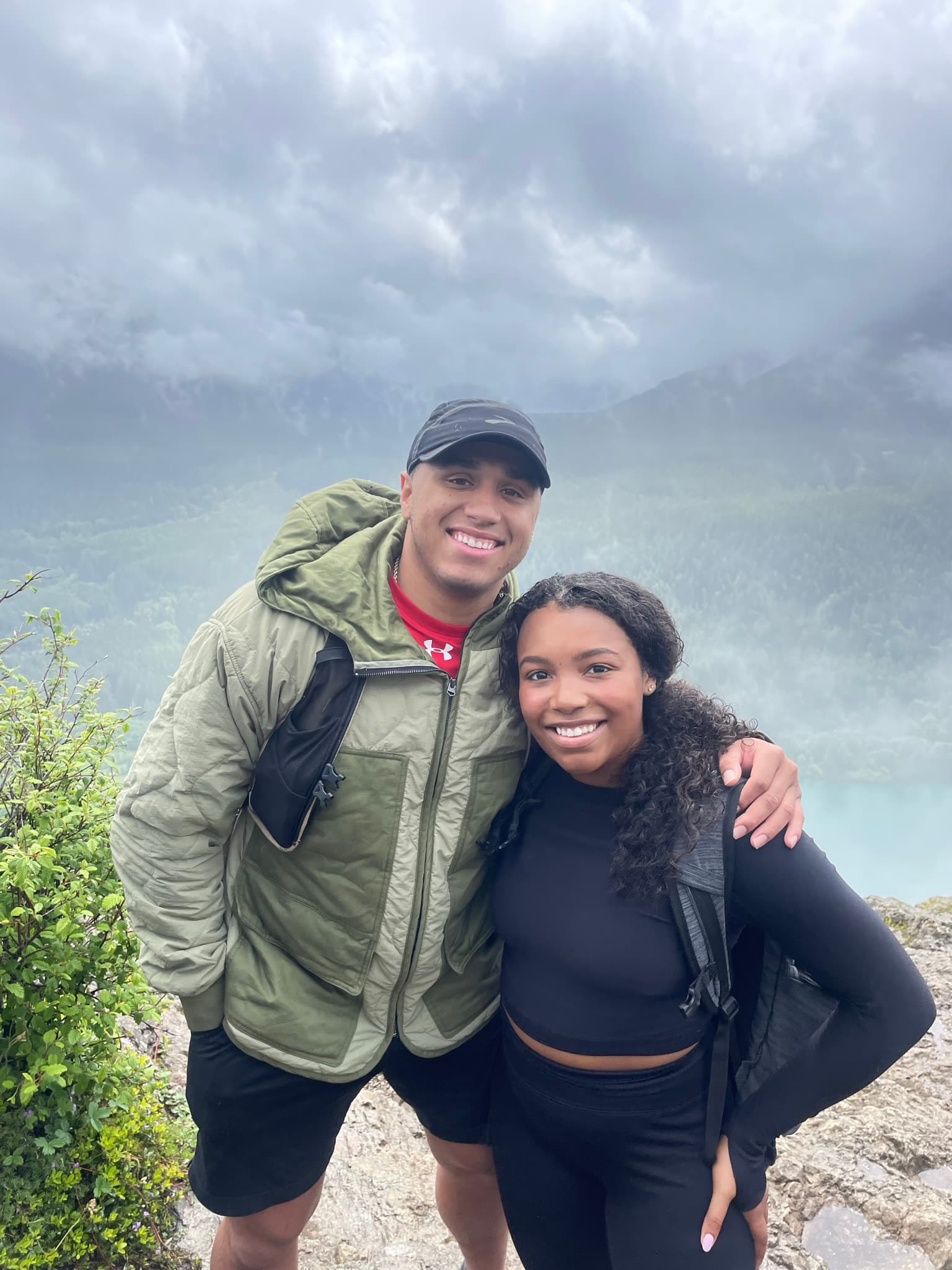 Cayla and Shaddy smiling together on a hike above a misty mountain lake.