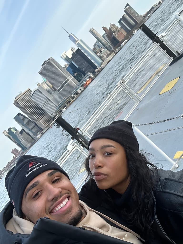 Cayla and Shaddy taking a selfie in knit hats with the waterfront skyline behind them.